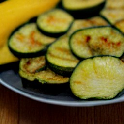 the grilled zucchini and summer squash are transferred to a plate.