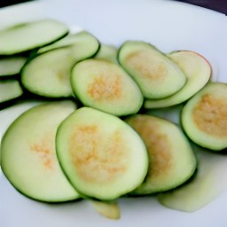 the marinated zucchini slices are transferred to a plate and sprinkled with black pepper and kosher salt.