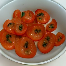 a bowl of tomato halves mixed with dried basil, olive oil, and black pepper.